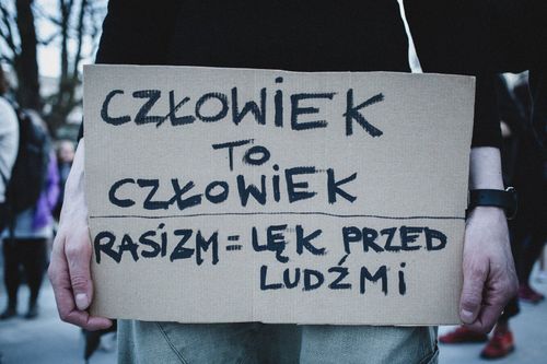 Zdjęcie osoby trzymającej kawałek kartonu z napisem "Człowiek to człowiek. Rasizm = lęk przed ludźmi"